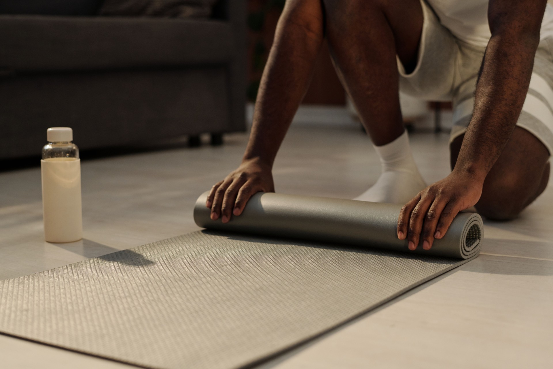 Close-up of hands of young man unrolling grey mat on the floor
